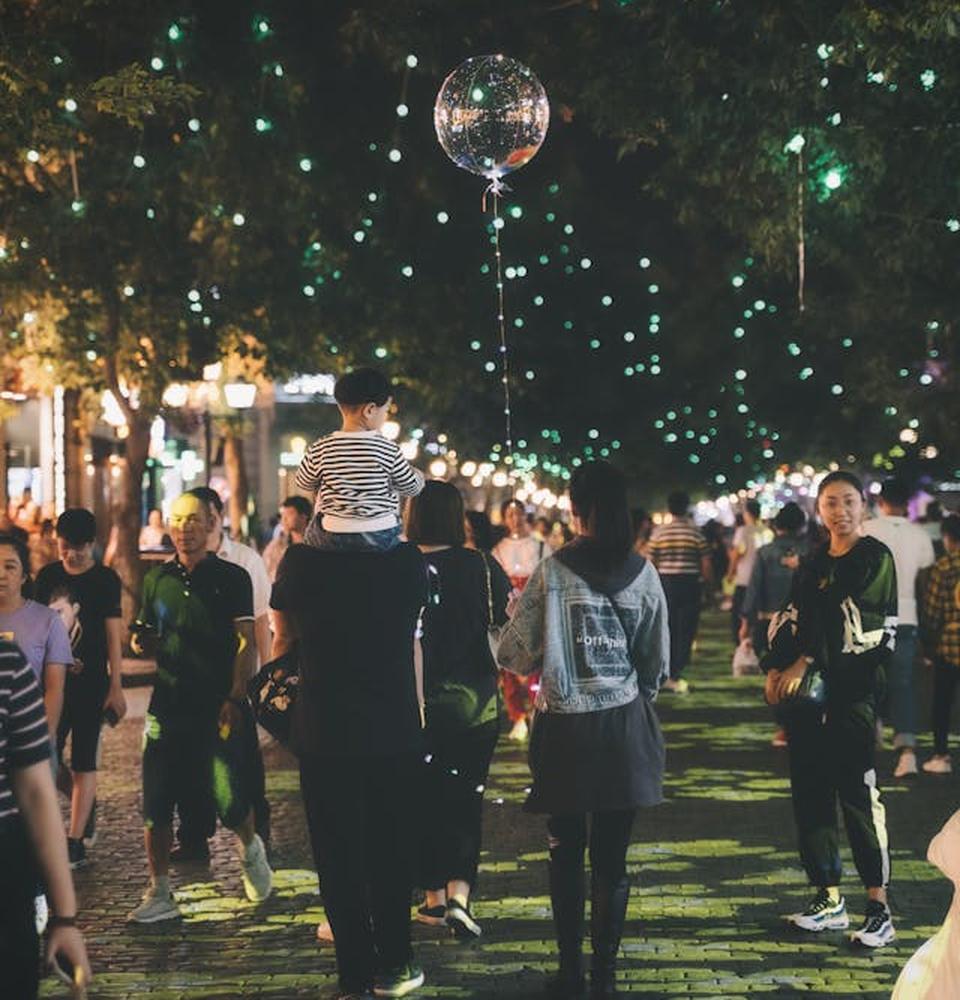 Menschen flanieren durch eine nächtliche Straße mit bunten Lichtern